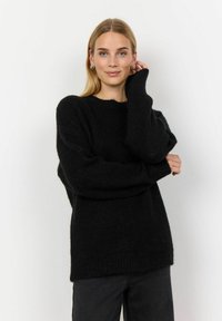 Pullover negru supradimensionat cu o textură cu dungi, mâneci largi și un tiv brut. Stilizat cu pantaloni negri cu talie înaltă pe un fundal simplu.