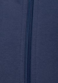 Marineblauwe zip-up kledingstuk met een gladde textuur, voorzien van een centrale rits en ribgebreide randen. Stof lijkt iets rekbaar.