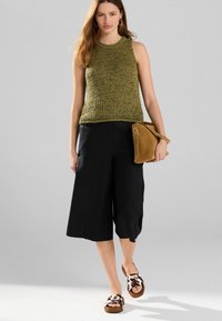 Grünes ärmelloses Stricktop, schwarze Culottes und braune Tasche. Sandalen mit braunem und weißem Muster. Einfaches Design, glatte Texturen.