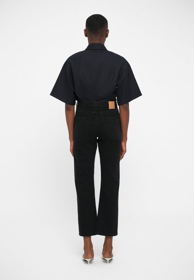 Pantalones de mezclilla negra con pierna recta y bolsillos traseros, combinados con una camisa de manga corta a rayas oscuras. Diseño simple y limpio, con cintura ajustada.