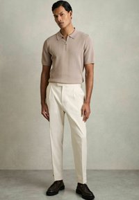 Polo din tricot bej cu fermoar, asortat cu pantaloni crem și pantofi maro cu șiret. Design slim-fit cu un finisaj texturat.