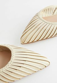 Chaussures blanches à bout pointu avec des découpes en cuir et des accents tissés autour de l'ouverture, présentant un intérieur lisse et une semelle plate.