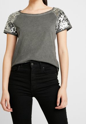 Gray short-sleeve top with sequin-embellished sleeves, round neckline, and soft texture. Paired with black high-waisted jeans.