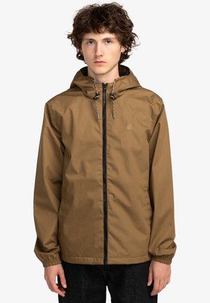 Chaqueta ligera marrón con capucha, cierre de cremallera y cordones ajustables; cuenta con puños elásticos y un logo simple en el pecho.