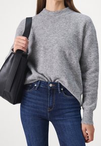 Suéter de lana gris con cuello redondo, corte relajado y puños de canalé, combinado con jeans de mezclilla azul oscuro y un bolso tote de cuero negro.