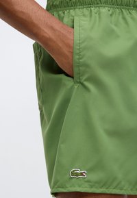 Πράσινα μαγιό σορτς από ελαφρύ, λείο ύφασμα. Διαθέτουν ελαστική μέση και μικρό κεντητό λογότυπο κροκοδείλου στο τελείωμα.