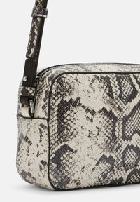 Borsa a tracolla in stampa serpente in bianco e nero, caratterizzata da una finitura in pelle strutturata, chiusura con zip e tracolla regolabile con accenti metallici.