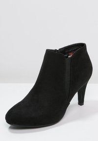 Stivale alla caviglia in suede nero con punta affusolata, tacco sottile e pannelli elasticizzati laterali per facilità di indossamento; presenta una texture liscia e un design semplice.