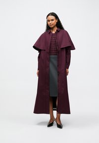 Garšs, bordo krāsas mētelis ar platām kapuci, ar rāvējslēdzēju un sānu šķirbēm. Valkāts virs strukturētas, tumšas blūzes un pieguļošām pelēkām svārkiem.