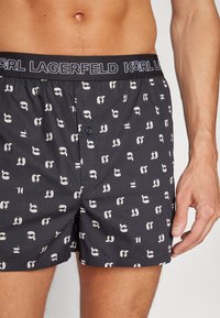 Pánské černé boxerky s opakujícími se bílými grafickými vzory. Měkká tkanina, elastický pas s logem "KARL LAGERFELD", přední zapínání na knoflík.