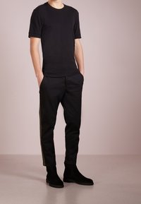 Black short-sleeve t-shirt paired with black tapered pants featuring olive green side stripes and black suede ankle boots.