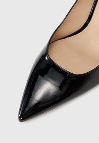 Zapato de tacón patentado negro con punta afilada y un diseño elegante, que presenta una superficie brillante y lisa con un forro interior minimalista.