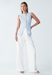 Helesinine ilma varrukat top viis nupuga, millel on terav äär. Kombineeritud tekstuuriliste valgete laiade pükstega ja minimalistlikud sandaalid.