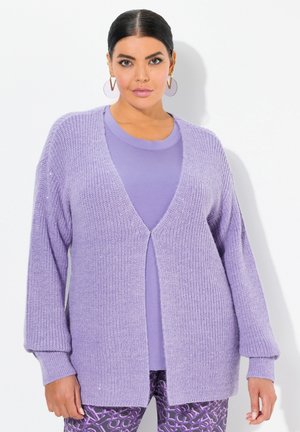 Helllila Strickjacke mit offenem Vorderteil, langen Ärmeln und lockerer Passform, kombiniert mit einem passenden lilafarbenen Top und gemusterten Leggings.