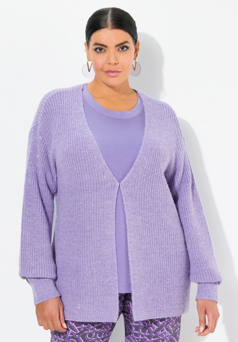 Ljust lila stickad cardigan med öppen framsida, långa ärmar och lös passform, parat med en matchande lila topp och mönstrade leggings.