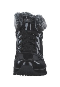 Botas sintéticas negras con un acabado brillante y Patent, borde de pelo sintético en el cuello, y cordones negros. Suela de goma con diseño para mayor tracción.