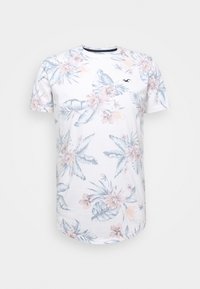 Vit bomulls-T-shirt med en ljusblå och pink tropisk blommönster, rund hals och korta ärmar. Diskret varumärkeslogo på bröstet.