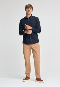 Mörk denimskjorta med knappar och långa ärmar, i kombination med ljusa khakibyxor och bruna sneakers. Enkelt design med minimala accenter.