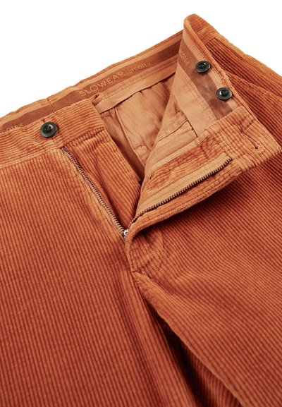 Spodnie sztruksowe w rdzawym pomarańczowym kolorze, z zamkiem błyskawicznym i zapięciem na guzik. Tkanina ma prążkowaną teksturę, z gładką podszewką.