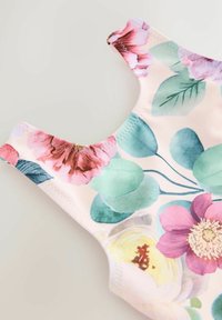 Beżowa tkanina bez rękawów w kwiatowy wzór z dużymi zielonymi liśćmi oraz różowymi, żółtymi i fioletowymi kwiatami na jasnym tle.