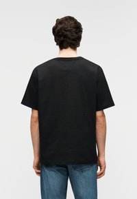 Μαύρο κοντομάνικο T-shirt με στρογγυλή λαιμόκοψη, φτιαγμένο από μαλακό βαμβάκι, με άνετη εφαρμογή και διακριτική υφή στο ύφασμα.