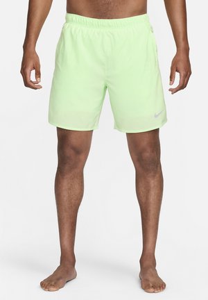 Homme portant un short de sport vert clair avec une ceinture élastique et un logo Nike sur la jambe gauche, debout pieds nus sur fond blanc.