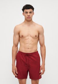 Pantaloni de baie maron cu talie elastică și șnur, având o textură netedă și lungime deasupra genunchiului; fără modele sau accente suplimentare.