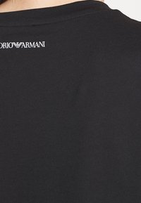 Černé bavlněné tričko s kulatým výstřihem, vyznačující se bílým logem "Emporio Armani" na zádech, hladkým povrchem a klasickým střihem.