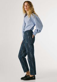 Light blue striped button-up shirt with puff sleeves, paired with dark blue patterned high-waisted trousers and black slip-on shoes.