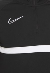 Black Nike half-zip pullover with a white horizontal stripe and logo on the left chest; smooth texture and athletic fit.