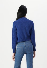 Pull bleu texturé coupé court avec manches longues et ourlet côtelé, associé à un jean bleu taille haute avec poches arrière.