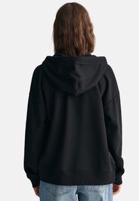 Sort oversized hættetrøje med hætte og lange ærmer, der har en blød tekstur og ribbede manchetter. Bæres med lyst vaskede denim.