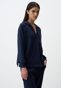 Pullover blu navy con cappuccio, scollo a V e maniche lunghe, caratterizzato da una vestibilità rilassata e fessure laterali. Realizzato in un tessuto morbido e texturizzato.
