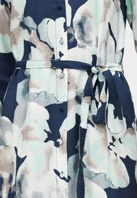 Φόρεμα με κουμπιά και αφηρημένο λουλουδένιο μοτίβο σε μπλε, μπεζ και ανοιχτό πράσινο, με ζώνη από ύφασμα που δένει στη μέση.