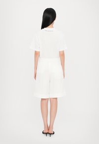 T-shirt en coton blanc à manches courtes, associé à un short blanc chegando au genou avec une poche arrière et une taille élastique. Talons noirs.