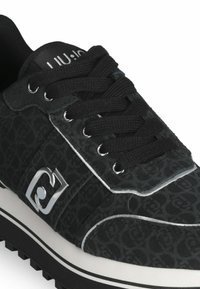 Sneaker nero con upper testurizzato caratterizzato da un motivo, dettagli argentati, lacci neri piatti e suola bianca con battistrada nero.
