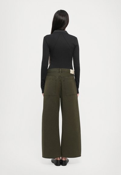 Zwarte top met lange mouwen en een getailleerd design, gecombineerd met olijfgroene wijde broek. De broek heeft een hoge taille en twee achterzakken.