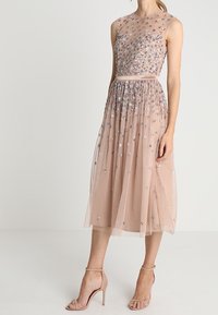 Un vestido sin mangas hasta la rodilla en suave tul de color rosa empolvado adornado con lentejuelas florales multicolores. Presenta un corsé ajustado y una falda fluida.