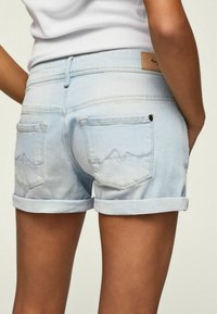 Jasnoniebieskie szorty dżinsowe z podwiniętymi nogawkami, z dwoma tylnymi kieszeniami i subtelnymi detalami haftu w kształcie gór na prawej kieszeni.