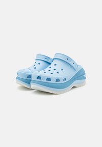 Lys blå klomper med ventilasjonshull, en konturert design, teksturert overflate og en hvit mellomsoff. Har en bakstropp for sikker passform.