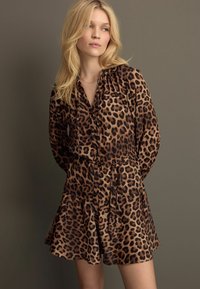 Leopardmönstrad klänning med långa ärmar, draperad halsringning, knappframstycke och utsvängd kjol. Tillverkad av ett mjukt tyg i bruna och svarta nyanser.