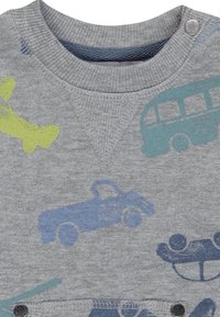 Sudadera gris con varios diseños impresos de vehículos, incluidos aviones, coches y autobuses, con broches de metal en el cuello.