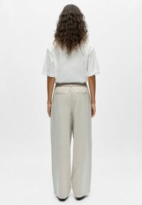 T-shirt blanc oversize à manches courtes associé à un pantalon large gris clair, doté d'une taille élastiquée avec cordon de serrage et de poches arrière.