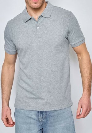 Polo shirt gris à manches courtes avec col, fabriqué en tissu doux. Il présente une patte de boutonnage à trois boutons et une texture subtile. Associé à un jean bleu clair.