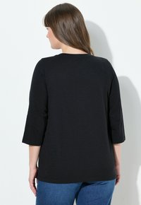 Haut noir à manches longues avec un col rond, texture lisse et coupe droite, associé à un jean en denim bleu.