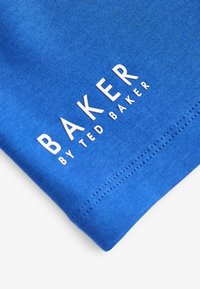 Modrá bavlnená látka s hladkým povrchom, na ktorej sa nachádza biele potlačené písmo "BAKER BY TED BAKER" a úhľadne prešitý lem.