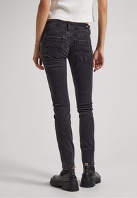 Černé úzké džíny s hladkou denimovou texturou, vybavené dvěma zadními kapsami s vlnkovým vzorem. Kombinované s černými kotníkovými botami.