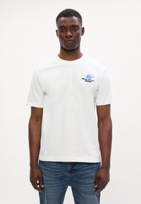 Valge puuvillane T-särk lühikeste varrukatega, millel on rinnaosas sinine graafikatekst ja kujundus. Pehme tekstuur ja lõdva stiiliga.