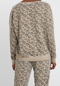 Sudadera de leopardo beige con un corte relajado y puños acanalados. Material suave con una textura sutil. Pantalones a juego completan el look.