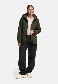 Olivgrön huva jacka med dragkedja, som har en avslappnad passform, två framfickor och ribbade ärmslut, kombinerad med svarta vida jeans.